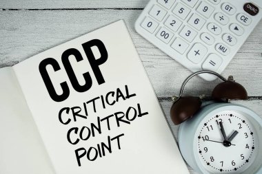 CCP Kritik Kontrol Noktası metni kağıt defter sayfasında alarm saati ve ahşap zemin üzerinde hesap makinesi ile