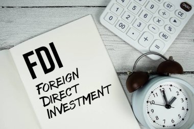 Kağıt defter sayfasında DDY Doğrudan Dış Yatırım metni alarm saati ve ahşap zemin üzerinde hesap makinesi ile