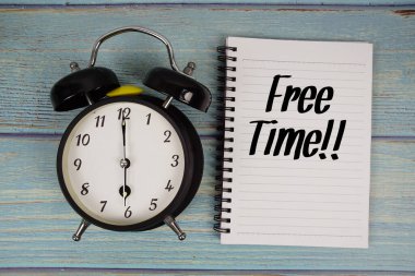 Boş zaman! Tahta zemin üzerinde alarmlı saat ile not defterine yazılmış metin