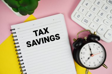 Hesap makinesiyle not defterine yazılmış Vergi Tasarruf metni ve pembe arkaplanda alarm saati