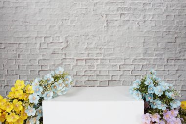 Beyaz kare podyum, beyaz tuğla duvar zeminli ürün sergisi için çiçek süslemesi
