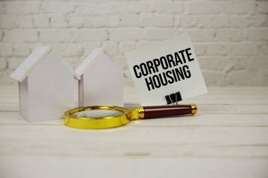 Kağıt üzerinde toplu konut mesajı, büyüteç ve ahşap arka planda ev modeli.