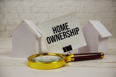 Ev sahiplerine ait mesaj kağıdı üzerinde büyüteç ve ahşap arka planda ev modeli var.