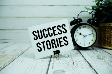 Başarı Öyküleri kağıt üzerinde, ahşap zemin üzerinde alarm saati olan metin