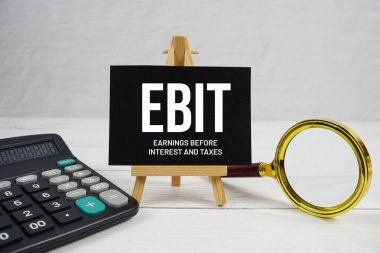 EBIT abbreviation of Earnings Before Interest and Taxes text with magnifying glass and calculator on wooden background