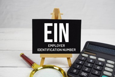 Ahşap zemin üzerinde büyüteç ve hesap makinesi olan EIN İşveren Kimlik Numarası metni