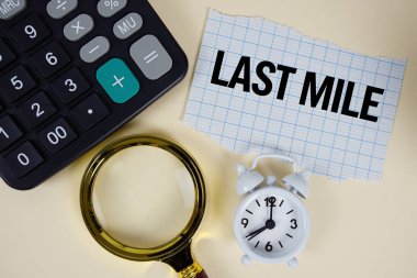 Last Mile text with alarm clock, magnifying glass anc calculator on yellow background