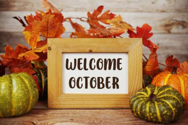 Ahşap zemin üzerinde akçaağaç yaprağı süslemesi olan Ekim ayına hoşgeldiniz metni