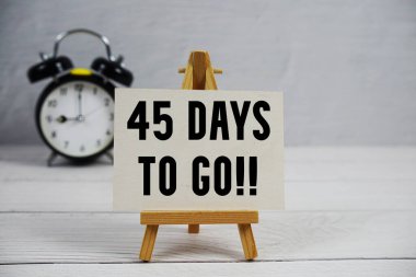 45 Gün kaldı! Ahşap arkaplanda resim sehpası ve alarm saati olan metin