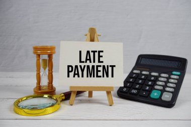 Tahta zemin üzerinde büyüteç ve hesap makinesi olan geç ödeme metni