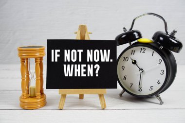 Eğer şimdi değilse. Ne zaman? Tahta zemin üzerinde kum saati ve alarm saati olan metin