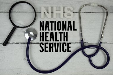 Ahşap zemin üzerinde steteskop bulunan NHS Ulusal Sağlık Servisi metni