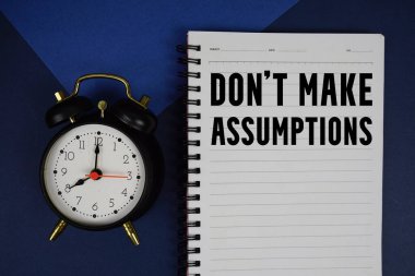 Not defterine mavi arkaplanda alarm saati yazılı varsayımlar yazma