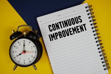 Not defterine yazılan ve sarı arkaplanda alarm saati olan sürekli geliştirme metni