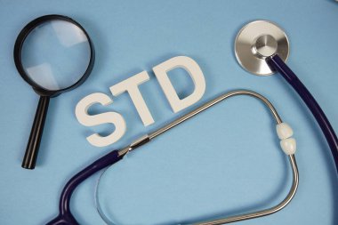 Cinsel yolla bulaşan hastalıkların kısaltması. Mavi arka planda büyüteç ve steteskop olan alfabe harfleri.