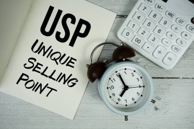 Kağıt defter sayfasında USP Eşsiz Satma Noktası metni. Alarm saati ve tahta zemin üzerinde hesap makinesi var.