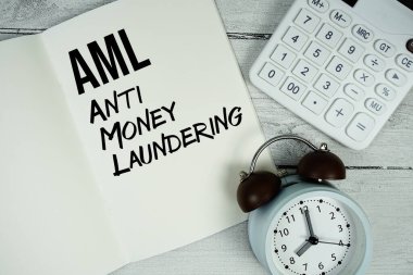 Kağıt defter sayfasında alarm saati ve tahta zemin üzerinde hesap makinesi olan AML Para Aklama Karşıtı metin