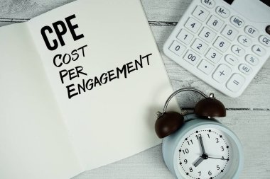 Kağıt defter sayfasında, alarm saati ve ahşap zemin üzerinde hesap makinesi olan ÇPE Başvuru Başına Maliyet metni