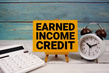 Kazanılan gelir kredi kartı metni hesap makinesi ve ahşap zemin üzerinde alarm saati ile birlikte kağıt kart üzerine yazıldı