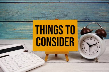 Hesap makinesi ve ahşap zemin üzerindeki alarm saati ile kağıt kartta yazılan metni dikkate alınacak şeyler