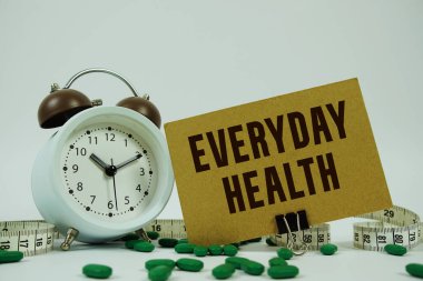 Her gün sağlık metni, ilaç, alarm saati ve beyaz arka planda mezura.