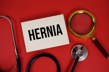 Fıtık metni kağıt kartta steteskop ve kırmızı arka planda büyüteç ile yazılmış.