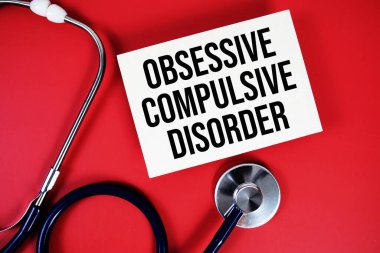 Takıntılı Kompülsif Bozukluk metni kağıt kartına yazılmış ve steteskop kırmızı arka planda.