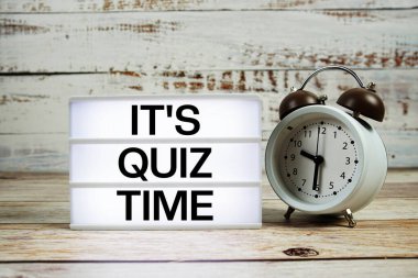 Tahta zemin üzerinde alarm saati olan ışık kutusuyla Quiz Time metni.