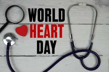 Tahta zemin üzerinde kırmızı kalp, büyüteç ve tıbbi stetoskop olan Dünya Kalp Günü metni
