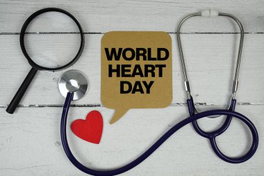Tahta zemin üzerinde kırmızı kalp, büyüteç ve tıbbi stetoskop olan Dünya Kalp Günü metni