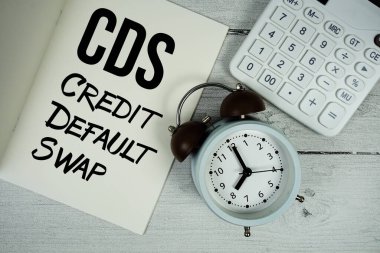 Kağıt defter sayfasında CDS Kredi Öntanımlı Takas metni alarm saati ve tahta arka planda hesap makinesi ile