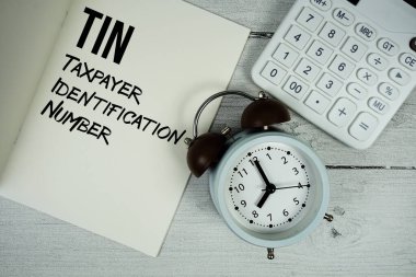 Kağıt defter üzerinde TIN Vergi mükellefi Kimlik Numarası metin, alarm saati ve ahşap zemin üzerinde hesap makinesi.