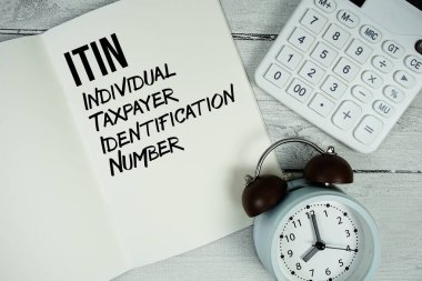 ITIN Bireysel Vergi Ödeyen Kimlik Numarası Kağıt defter sayfasında alarm saati ve ahşap zemin üzerinde hesap makinesi olan metin
