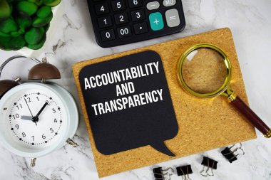 Hesap Makinesi, çalar saat ve mermer zemin üzerinde büyüteç içeren Saygınlık ve Şeffaflık metni