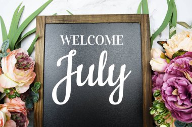 Mermer zemin üzerine süslenmiş çiçeklerle karatahtaya Temmuz ayına hoşgeldiniz