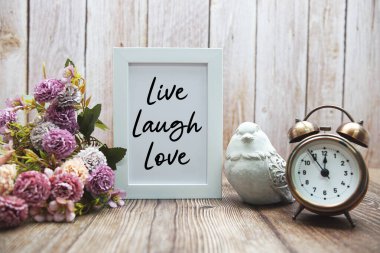 Ahşap arka planda çiçek desenli Live Laugh Love metni