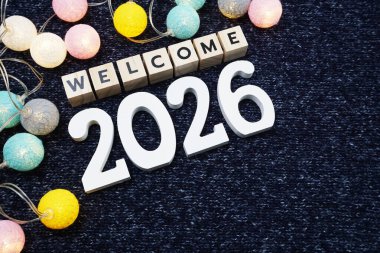 Mavi örülmüş kumaş zemin üzerinde LED pamuk topu olan 2026 alfabe mektubuna hoş geldiniz