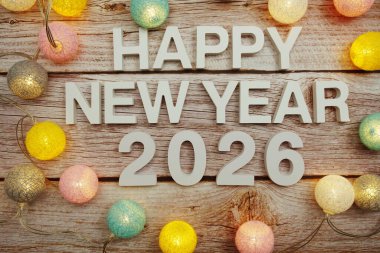Yeni yılınız kutlu olsun 2026 alfabesi. Ahşap zemin üzerinde LED pamuk topları ile süsleyin.