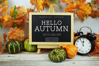 Sonbahar İndirimi% 10 alarm saati ve ahşap arka planda akçaağaç yaprağı süslemesi içeren metin