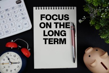 Focus On The Long Term Investment text with calculator with alarm clock and piggy bank on black background