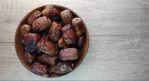 Dates fruit in a wooden bowl on a wooden background. Top view.