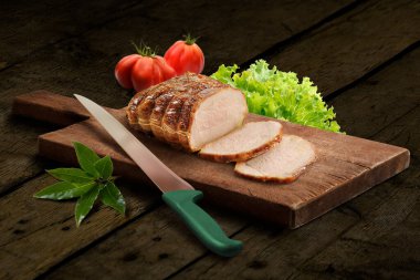 Wooden chopping board with roasted sliced meat and knife on rustic wood