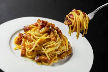 Siyah taş arka planda spagetti carbonara ile çatal ve tabak.