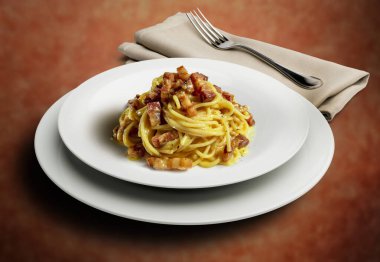 Kırmızı benekli arka planda çatal ve peçeteli spagetti alla carbonara ile kalın tabak.