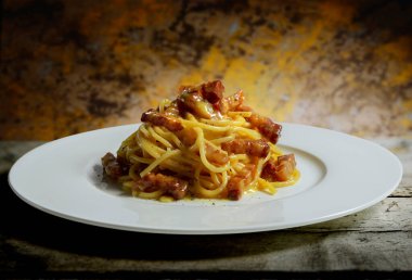 Bir tabak spagetti carbonara kaba ahşap masada izole edilmiş.