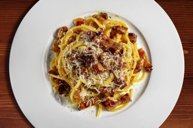 Tabağın üst görüntüsünü spagetti carbonara ve rendelenmiş peynir ile ahşap arka planda detaylandır