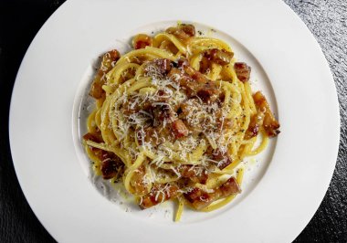 Tabağın üst görüntüsünü spagetti carbonara ve rendelenmiş peynirle birlikte siyah taş arka planda detaylandır