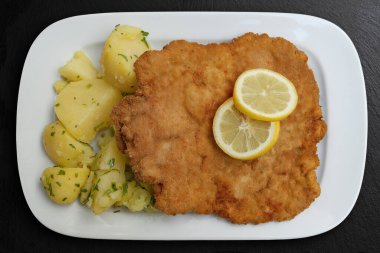 Top view of Schnitzel Classisc Viennese Veal Cutlet with potato salad and lemon slices on black stone clipart