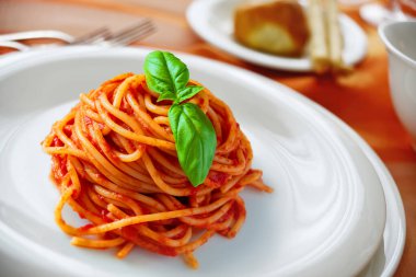 Plate with spaghetti with tomato and basil on a laid table clipart