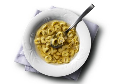 Çorba kasesinin üst görüntüsü tortellini ile beyaz arka planda peçete ve kaşıkla çorba.